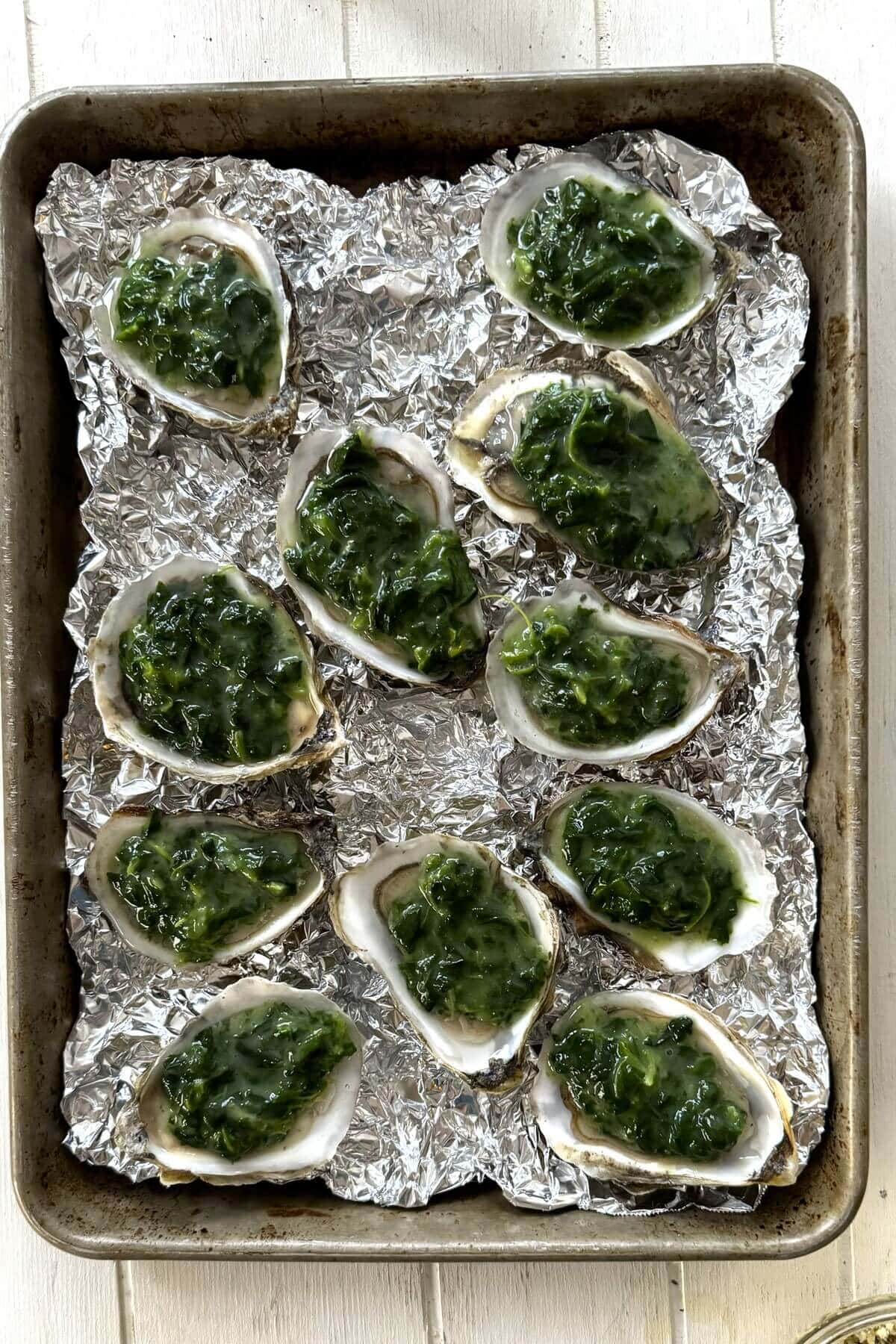 Shucked oysters topped with creamed spinach on a baking sheet.