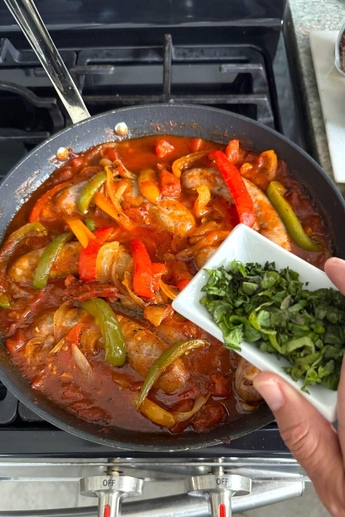 Adding fresh chopped basil to Italian sausage and peppers.