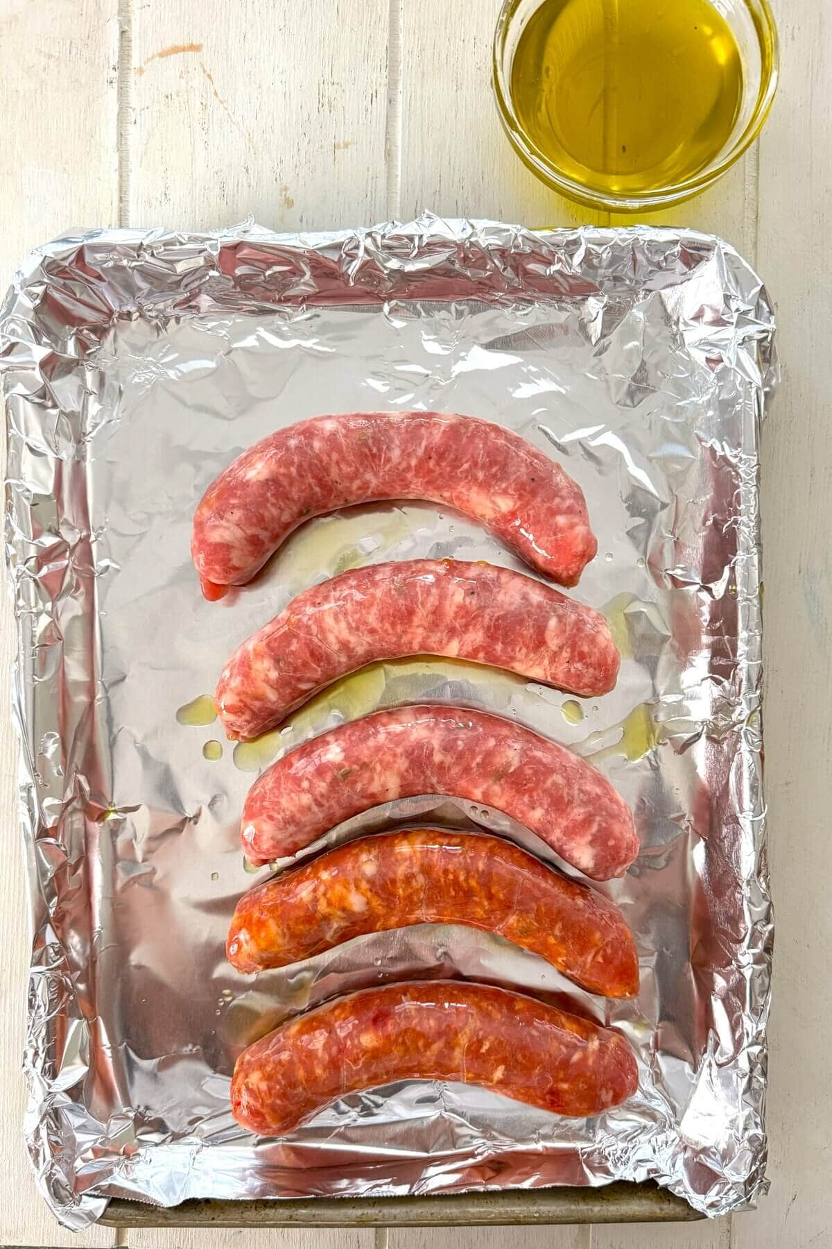 Raw Italian sausages on a foil lined baking sheet.