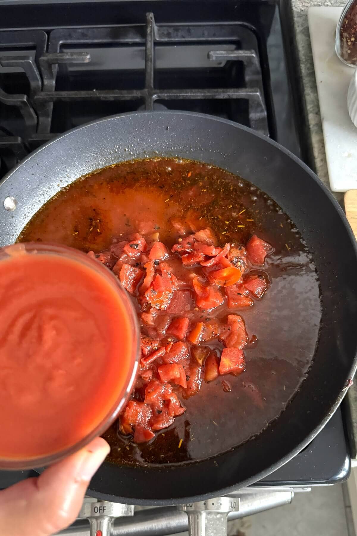 Adding tomato sauce to sausage and peppers sauce.