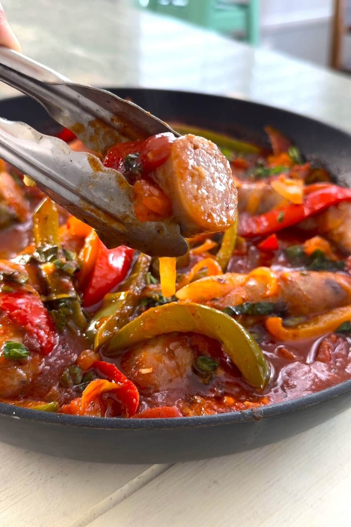 A slice of cooked Italian sausage and a skillet of sausage and peppers.