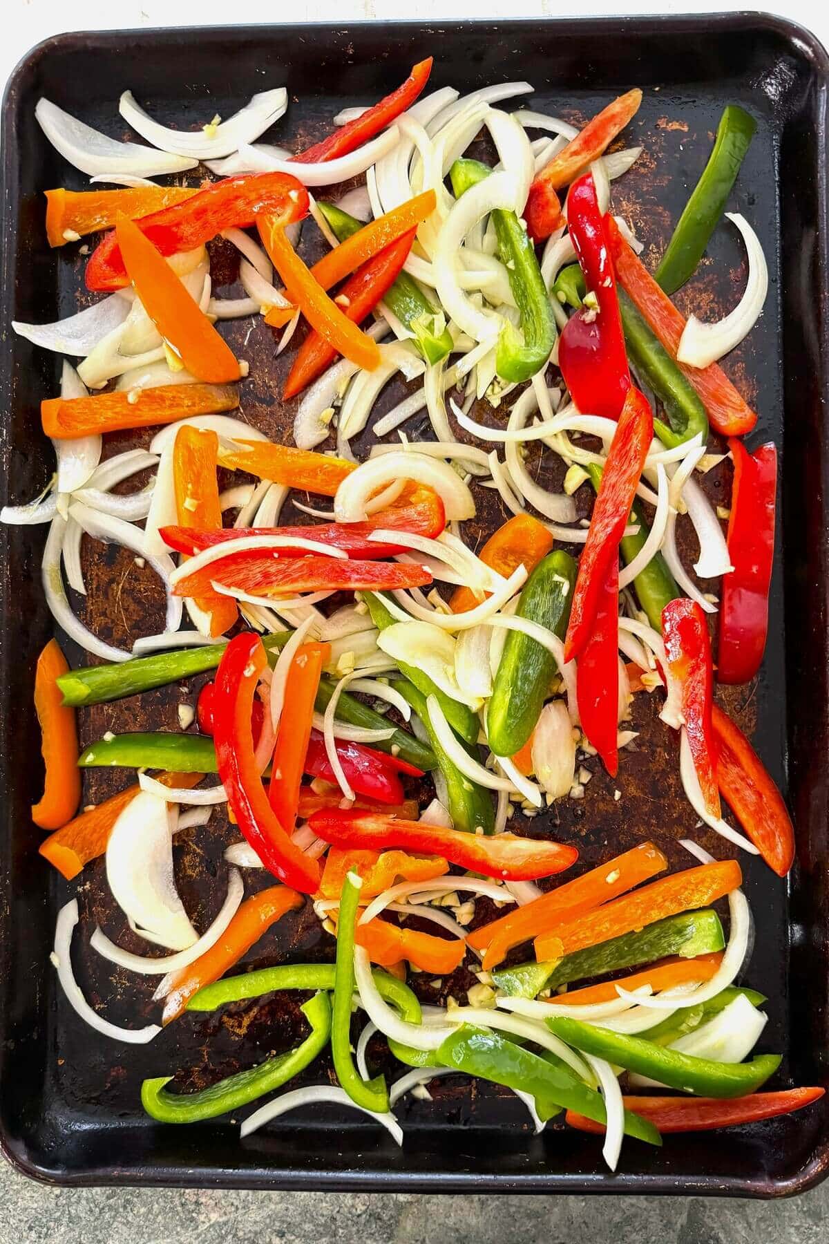 Sliced bell peppers, onions and garlic on a baking sheet.